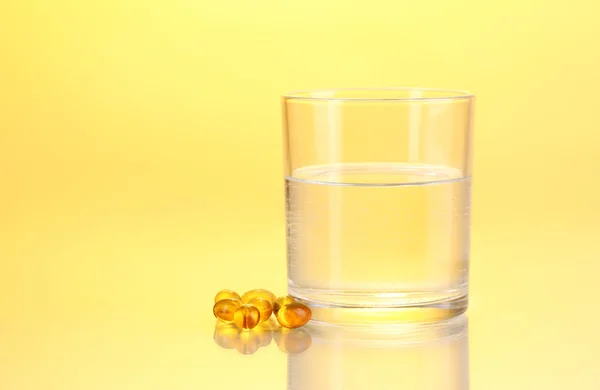 Szklanką wody i tabletki na żółtym tle — Zdjęcie stockowe