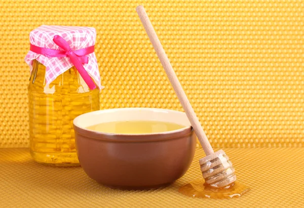 Jar of honey, bowl and wooden drizzler with honey on yellow honeycomb backg — Stock Photo, Image