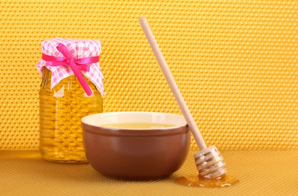 stock image Jar of honey, bowl and wooden drizzler with honey on yellow honeycomb backg