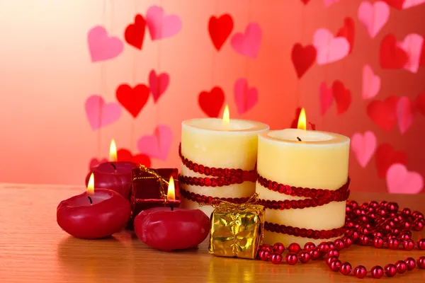 Красиві свічки з романтичним декором на дерев'яному столі на червоному тлі — стокове фото