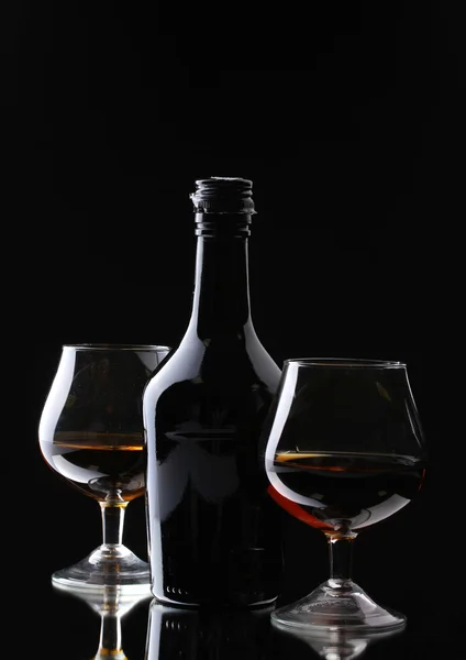 Glazen van brandy en fles op zwarte achtergrond — Stockfoto