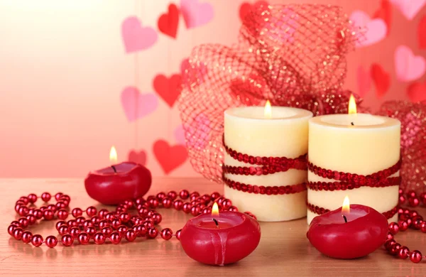 Красивые свечи с романтическим декором на деревянном столе на красном фоне — стоковое фото
