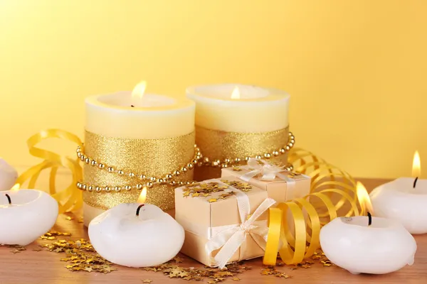 Belas velas, presentes e decoração em mesa de madeira no fundo amarelo — Fotografia de Stock