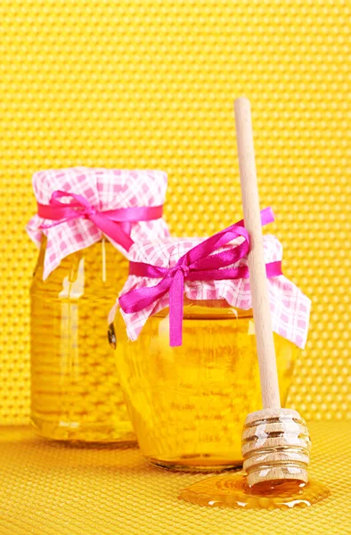 Jars of honey and wooden drizzler on yellow honeycomb background Stock Photo
