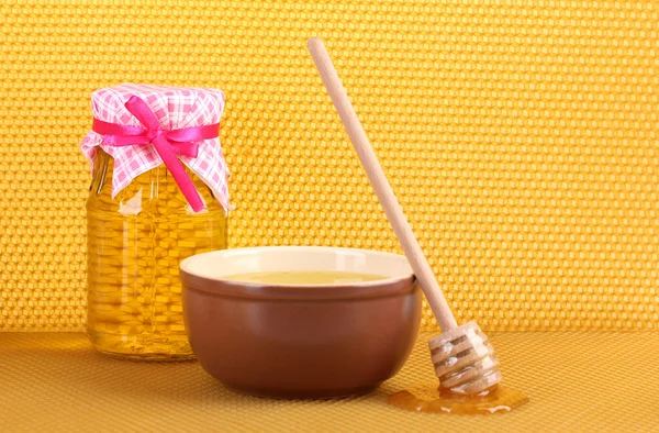 Jar of honey, bowl and wooden drizzler with honey on yellow honeycomb backg Stock Photo