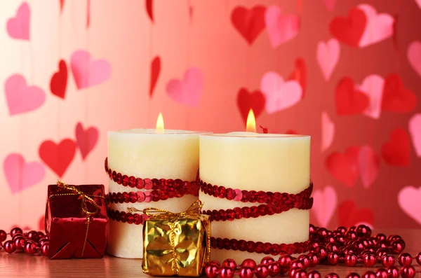 Beautiful candles with romantic decor on a wooden table on a red background Stock Image