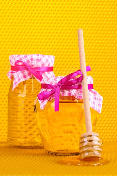 Jars of honey and wooden drizzler on yellow honeycomb background Stock Image