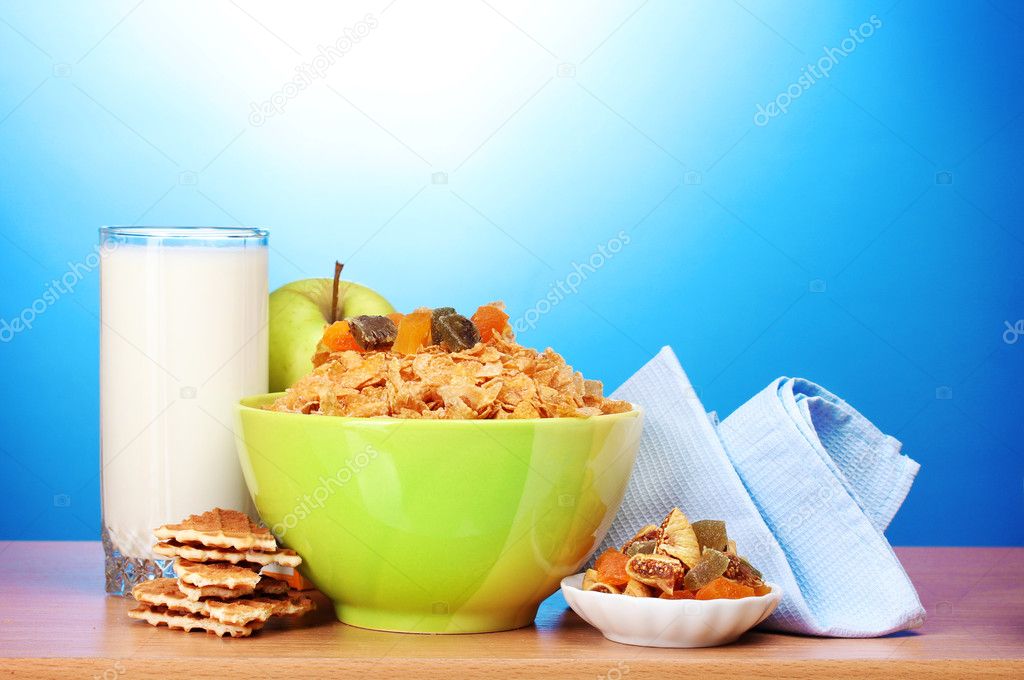 Tasty cornflakes in green bowl, apples and glass of milk on wooden table on