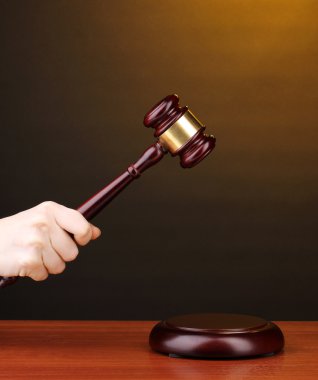 Judge's gavel in hand on brown background clipart