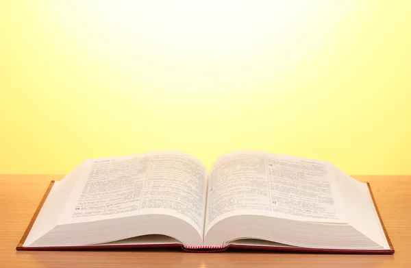 Açık kitap üzerine Sarı zemin üzerine ahşap masa — Stok fotoğraf