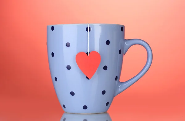 Xícara azul e saco de chá com rótulo vermelho em forma de coração no fundo vermelho — Fotografia de Stock