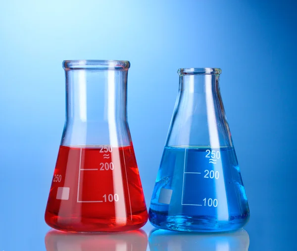Zwei Kolben mit roter und blauer Flüssigkeit mit Reflexion auf blauem Hintergrund — Stockfoto