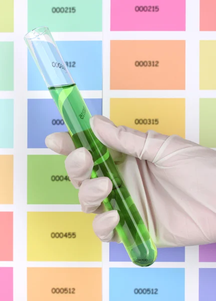 Трубка с зеленой жидкостью в руке на фоне цветных образцов — стоковое фото