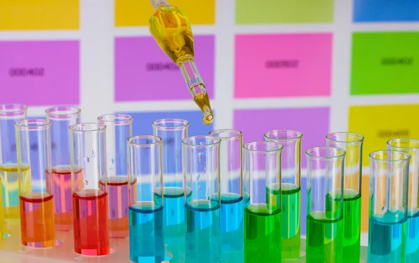Тестовые трубки с цветной жидкостью и пипеткой на фоне цветных образцов — стоковое фото