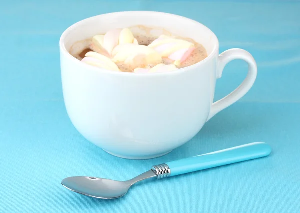 Cup of cappucino with marshmallows and spoon on blue background — Stock Photo, Image