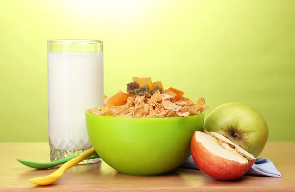 Tasty cornflakes in green bowl, apples and glass of milk on wooden table on — Stock Photo, Image
