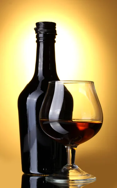 Sklenici brandy a láhev na žlutém podkladu — Stock fotografie
