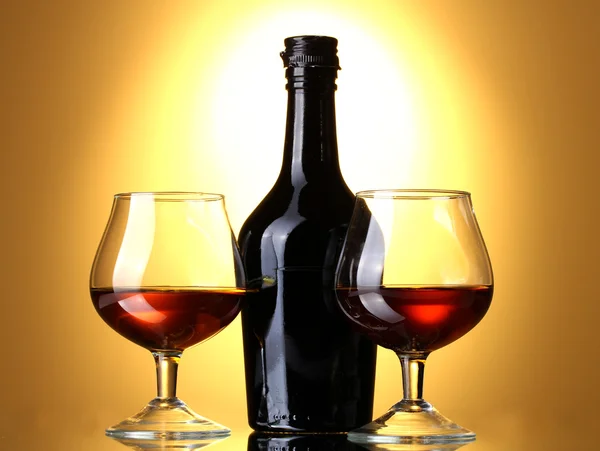 Gläser Schnaps und Flasche auf gelbem Hintergrund — Stockfoto