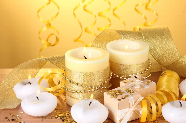 Belas velas, presentes e decoração em mesa de madeira no fundo amarelo — Fotografia de Stock