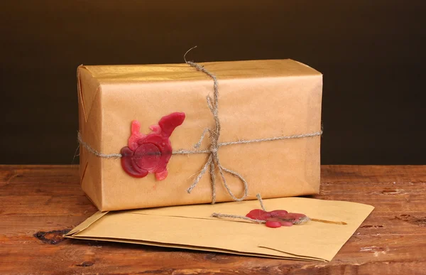 Посылка и конверт с герметичным воском на деревянном столе на коричневом фоне — стоковое фото