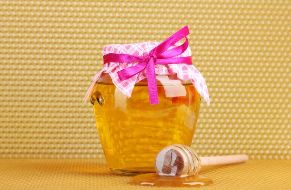 Jar of honey and wooden drizzler on yellow honeycomb background Royalty Free Stock Photos