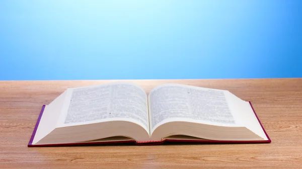 Открытая книга на деревянном столе на синем фоне — стоковое фото