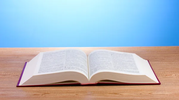 stock image Open book on wooden table on blue background