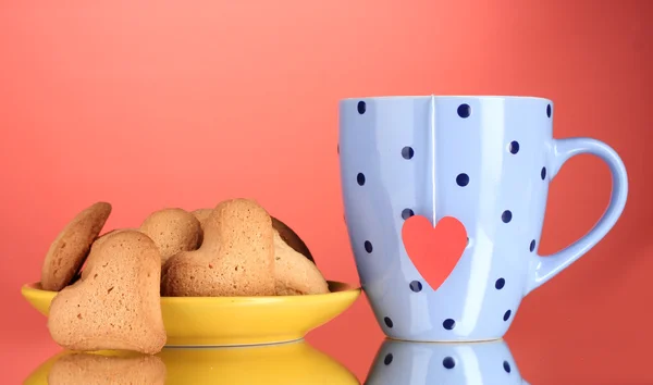Herzförmige Kekse auf gelbem Teller und Tasse mit Teebeutel auf rotem Hintergrund — Stockfoto