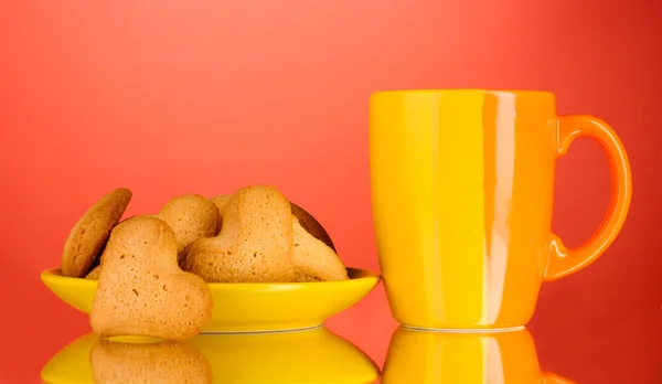 Heart-shaped cookies on yellow plate and cup on red background — Stock Photo, Image