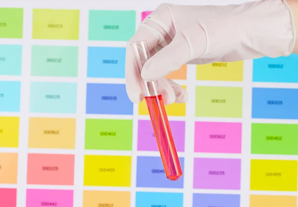 Tubo con líquido rojo en la mano sobre el fondo de muestras de color —  Fotos de Stock