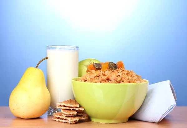 Välsmakande cornflakes i grön skål och glas mjölk på träbord på blå ba — Stockfoto