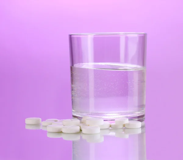 Bicchiere di acqua e pillole su sfondo viola — Foto Stock