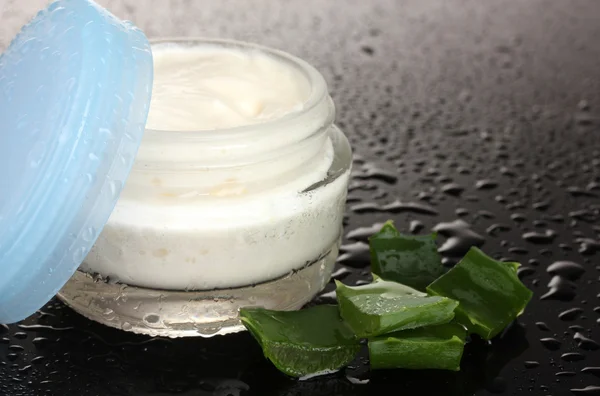 Opened glass jar of cream and aloe on black background with water droplets — Stock Photo, Image