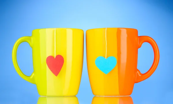 Two cups and tea bags with red and blue heart-shaped label on blue backgrou — Stock Photo, Image