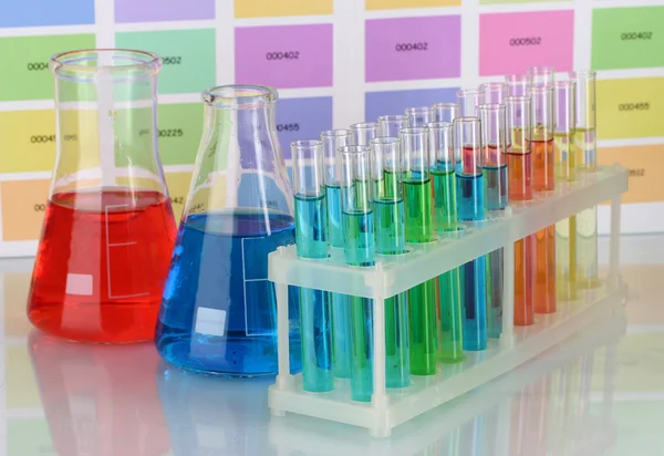 Tubos de ensaio e frascos com líquido de cor sobre fundo de amostras de cor — Fotografia de Stock