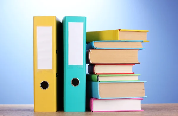 Helle Büromappen und Bücher auf Holztisch auf blauem Hintergrund — Stockfoto