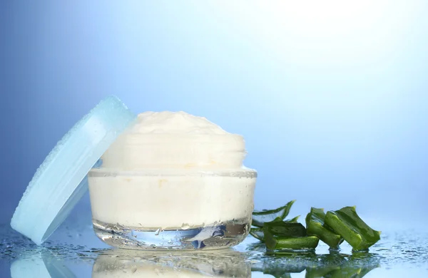 Vaso di vetro aperto di crema e aloe su sfondo blu con goccioline d'acqua — Foto Stock