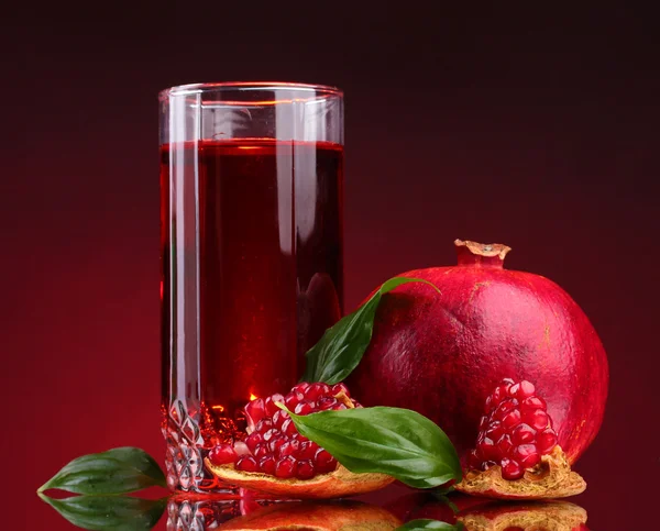 stock image Ripe pomergranate and glass of juice on red background