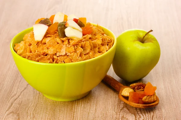 Välsmakande cornflakes i skål med torkad frukt och äpple på träbord — Stockfoto