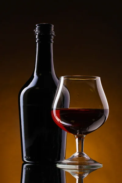 Kieliszek brandy i butelka na brązowym tle — Zdjęcie stockowe