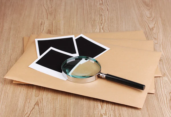 Enveloppen met fotopapier en vergrootglas op houten achtergrond — Stockfoto