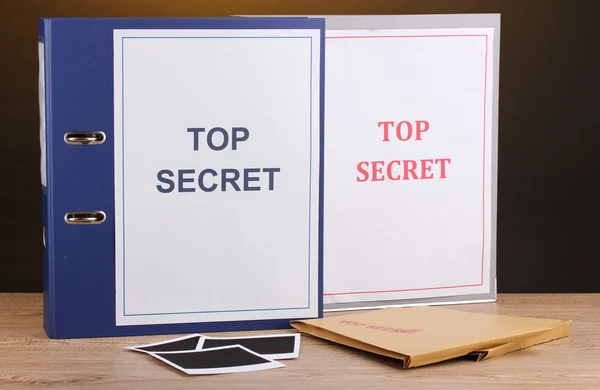 Enveloppen en mappen met top geheime stempel en foto papieren op houten tabl — Stockfoto