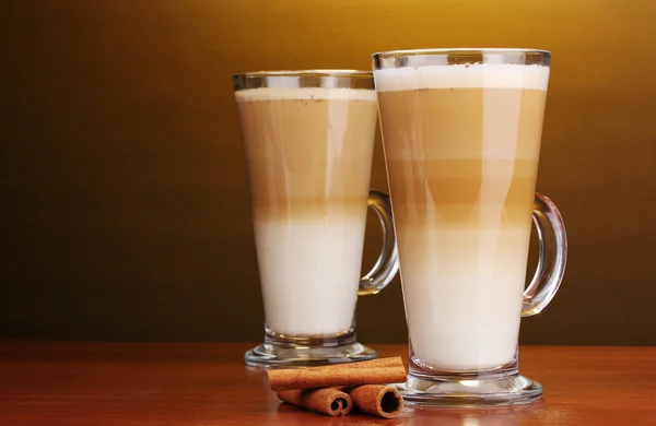 Duftender Kaffee-Latte in Glasbechern und Zimt auf Holztisch auf braunem B — Stockfoto