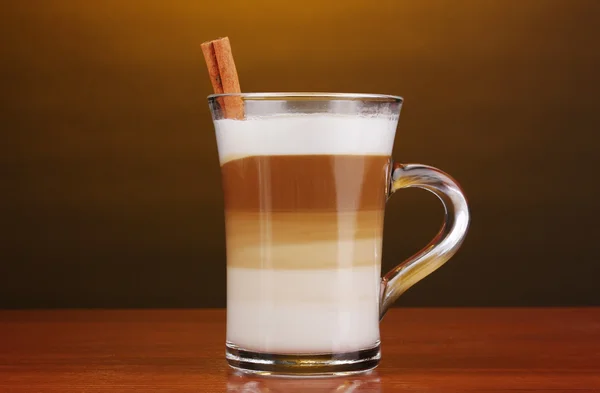 Café con leche fragante en taza de vidrio y canela en mesa de madera en la frente —  Fotos de Stock