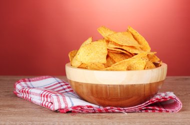 Tasty potato chips in wooden bowl on wooden table on red background clipart