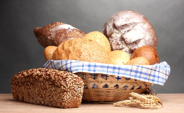Смачний хліб у кошику та вухах на дерев'яному столі на сірому фоні — стокове фото