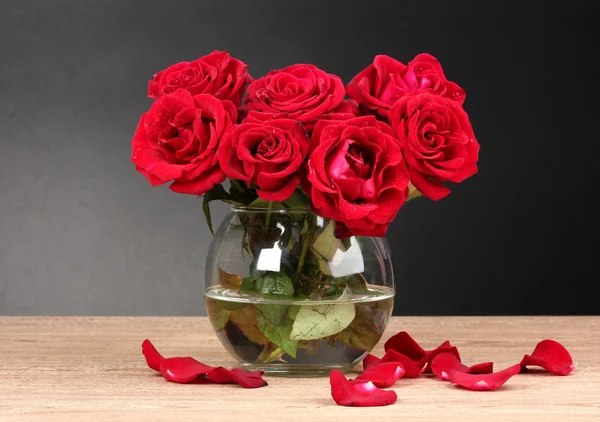 Schöne rote Rosen in Vase auf Holztisch auf grauem Hintergrund — Stockfoto