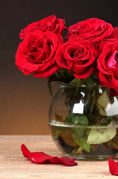 Krásné červené růže ve váze na dřevěný stůl na hnědé pozadí — Stock fotografie