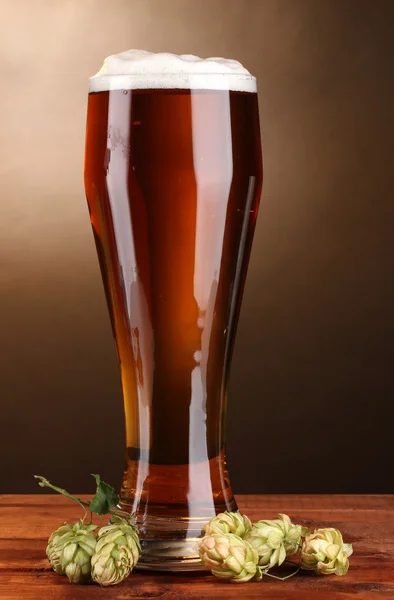 Пиво в склі і зелений хміль на дерев'яному столі на коричневому фоні — стокове фото