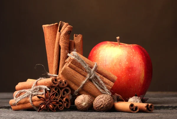 Laski cynamonu, czerwone jabłko, gałka muszkatołowa, anyż na drewnianym stole na tle brązowy — Zdjęcie stockowe